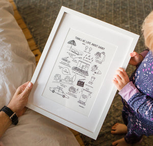 Little girl holding a white frame with adult holding the other side. The print in the frame is called 'things we love about daddy and includes a series of drawings.